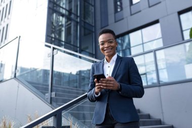 İş kadını cep telefonuyla eğlenmeyi ve gülümsemeyi sever. Ofis dışında takım elbiseli, Afro-Amerikan iş kadını.
