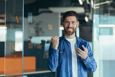 Sakallı mutlu bir iş adamı, profesyonel bir kazanan, akıllı telefondan iyi haberler okuyarak başarıyı kutlayan, cep telefonuyla mesajlaşma konusunda heyecanlı.