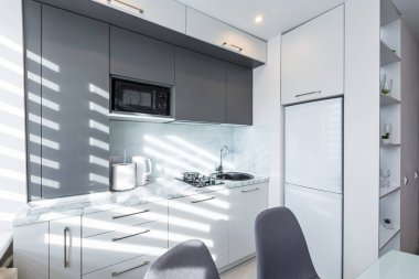 Beyaz ve gri küçük bir mutfağın içinde, yemek masası da var.