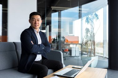 Başarılı bir işadamı olan patron kameraya bakıp gülümsüyor ve modern ofiste çalışıyor.