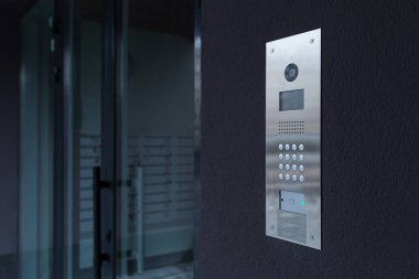 Entrance doorbell in a multi-apartment building, with a video surveillance camera, on a dark wall clipart