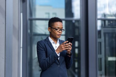 İş kadınının telefon kullandığını düşünen, ofisin yakınında takım elbiseli Afro-Amerikan bir kadın.