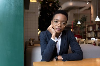 Afro-Amerikalı bir kadın bir kafede otururken ciddi bir iş kadını pencereden dışarı bakıyor.