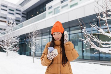 Kampüste genç bir kız öğrenci, Asyalı kış karlı bir günde müzik dinliyor, neşeli ve mutlu.