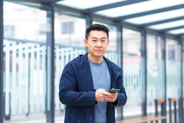 Thinking Asian, business man uses phone, near modern office, and airport