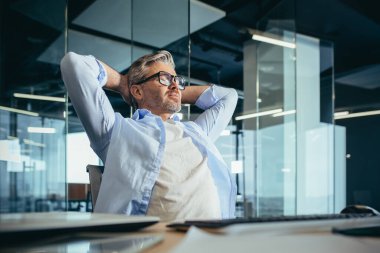 Düşünceli ve hayalperest iş adamı patronu, işte oturuyor, ellerini başının arkasına atıyor, dinleniyor.