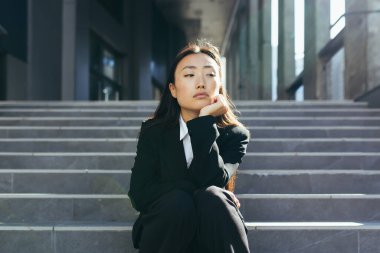Genç, güzel Asyalı kadın üzgün ve üzgün. Ofis merkezinin merdivenlerinde oturuyor. Depresyondaki iş kadını kovuldu.