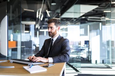 Portrait of businessman with beard, happy man working in office successful boss working at computer in modern office