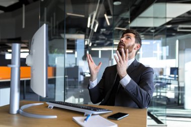 Businessman in despair asks for help, raising his hands up, asks God for success, man works in the office at the computer