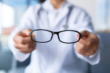 Close-up photo of doctor's hands holding eyeglasses, ophthalmologist offers glasses to patient