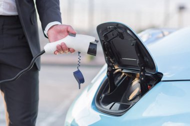 close-up photo of a male hand of a businessman charges an electric car, connects the charging cable