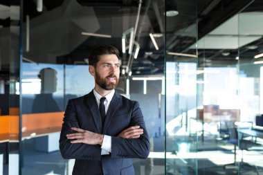 Successful business owner in a modern office, man with his hands folded on the cross, looks away and smiles