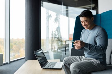 Asian businessman works in a modern office, a man holds a phone in his hands, and rejoices, reads the good news from the phone