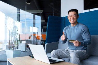 Asian man happy and smiling, businessman looking at camera and holding credit card for shopping in online stores