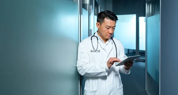 Médico Asiático Serio Utiliza Una Tableta Hombre Trabaja Una Clínica — Foto de Stock