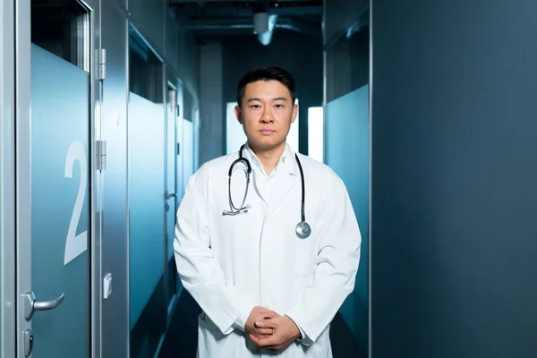 病棟近くの廊下でカメラをじっくり見つめていたアジア系の医師の肖像画です — ストック写真