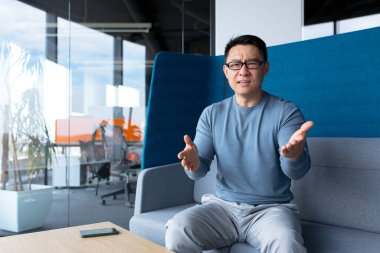 angry and serious asian man talking on video call, freelancer looking at webcam, businessman working in modern office