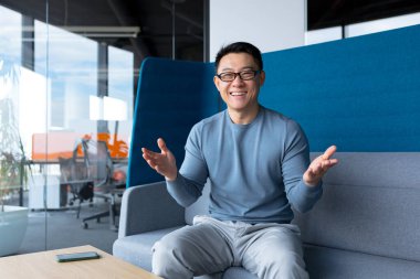 Cheerful teacher looks at the webcam, conducts online classes, Asian man works remotely