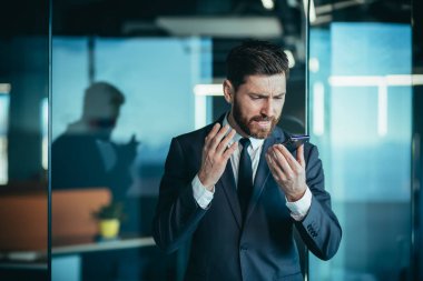 Angry and nervous boss shouting into phone, during phone conversation with employee, businessman in modern office with phone