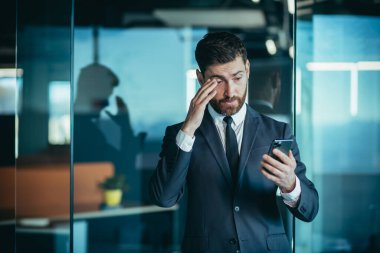 Angry and nervous boss shouting into phone, during phone conversation with employee, businessman in modern office with phone
