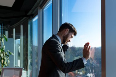 İflas etmiş işadamı patronu, pencereden dışarı bakıyor, takım elbiseli adam, modern ofiste depresyonda ve hayal kırıklığına uğramış.