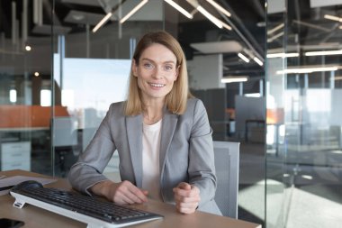 Portrait of beautiful business woman looking at camera and smiling, video call with colleagues, businesswoman working in modern office at computer