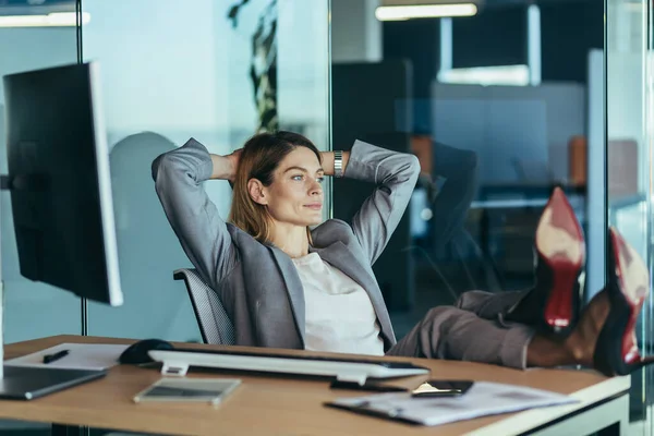 Woman director resting and dreaming at work, business woman throwing her hands behind her head and feet on the table, resting on the day at work