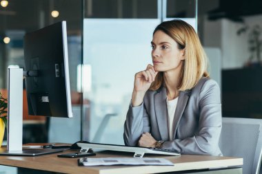 Thinking business woman looking at computer monitor, business woman working in modern office, planning new project, and business strategy