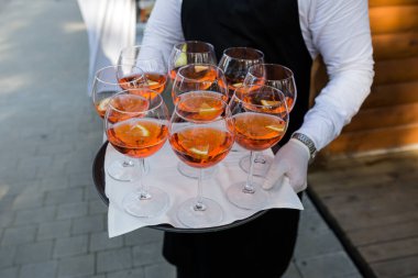 Garson misafirleri karşılar, yakın plan bir fotoğrafta gözlüklü Aperol içer.