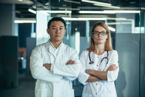 在诊所工作的严肃而专注的医生 手挽手 看着摄像机 亚洲男人和女人的团队 — 图库照片