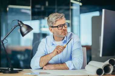 Deneyimli tasarımcı masada çalışıyor. Evin taslak planını çiziyor. Bir adam monitöre bakıyor.