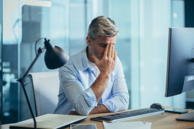 Mutsuz, gri saçlı mimar bilgisayarın modern ofisinde çalışıyor. İşadamı başarısızlıkları düşünüyor.