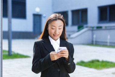 Güzel bir Asyalı öğrenci üniversite kampüsünün yanındaki telefonu kullanıyor.