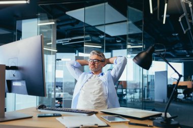 Düşünceli ve hayalperest iş adamı patronu, işte oturuyor, ellerini başının arkasına atıyor, dinleniyor.