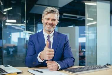 Tecrübeli bir yönetici kameraya bakar ve gülümser, bir iş adamı bir video görüşmesine el çırpar, bu da araya girenlere övgü ve destek göstergesidir.