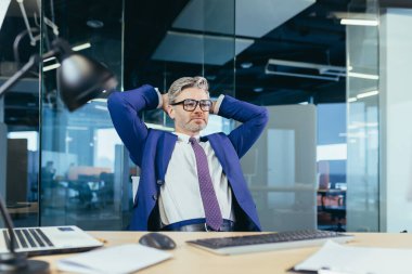 Düşünceli ve hayalperest iş adamı patronu, işte oturuyor, ellerini başının arkasına atıyor, dinleniyor.