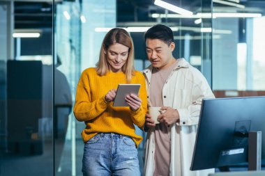 İki çalışan eğleniyor. Mola sırasında Asyalı bir adam ve sarışın bir kadın, meslektaşları modern bir ofiste birlikte çalışıyorlar, birlikte tablet bilgisayarlara bakıyorlar.