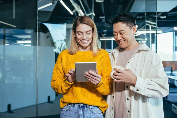 İki programcı arkadaş, bir erkek ve bir kadın, mutlu ve gülümsüyor tablet ekranına bakıyor, modern bir ofiste çalışıyor, öğle yemeği molası veriyor.