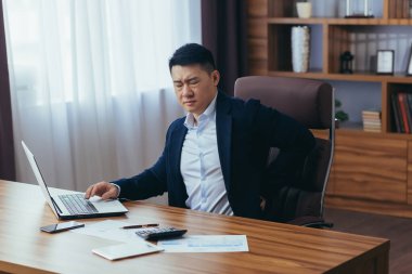 Bilgisayarın ofisinde çalışan iş adamı, Asyalı 'nın sırt ağrısı var, patron klasik bir ofiste, yeniden çalışıyor.