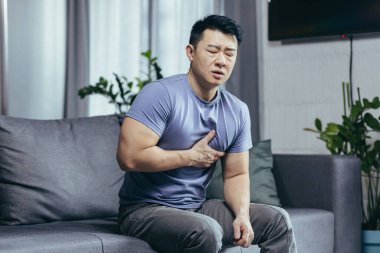 Oturma odasındaki kanepede oturan bir adam, Asyalı bir hasta ağır göğüs ağrısı, kalp rahatsızlığı.