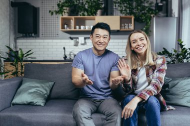 Mutlu çift webcam 'e bakıyor ve internette arkadaşlarıyla gülümsüyor. Farklı ırklardan erkek ve kadınlar el sallayarak tebrik ediyor, evde kanepede oturuyor.