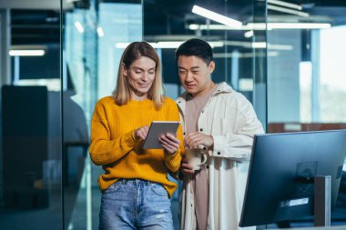 İki programcı arkadaş, bir erkek ve bir kadın, mutlu ve gülümsüyor tablet ekranına bakıyor, modern bir ofiste çalışıyor, öğle yemeği molası veriyor.