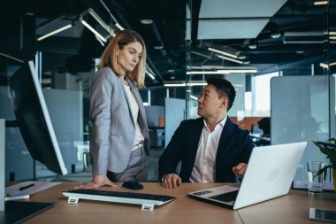 Mutlu iş arkadaşları proje stratejisini dizüstü bilgisayarın monitör ekranına bakarak tartışıyor. Ofiste çok ırklı iş adamları var. Genç bir kadını açıklayan kendinden emin Asyalı bir adam.