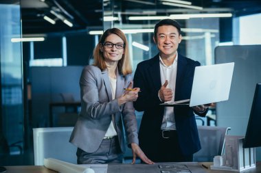 İki mimar ekibi, kameraya bakıyor ve tamamlanmış projeye gülümsüyor, olumlu bakmaya devam ediyorlar.