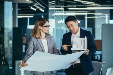 Grup genç yaratıcı mühendisleri yeni projeyi tartışıyor ofiste bir plan okuyor. Takım mimarı Asyalı erkek ve kadın meslektaşları model bina kullanarak konuşuyor