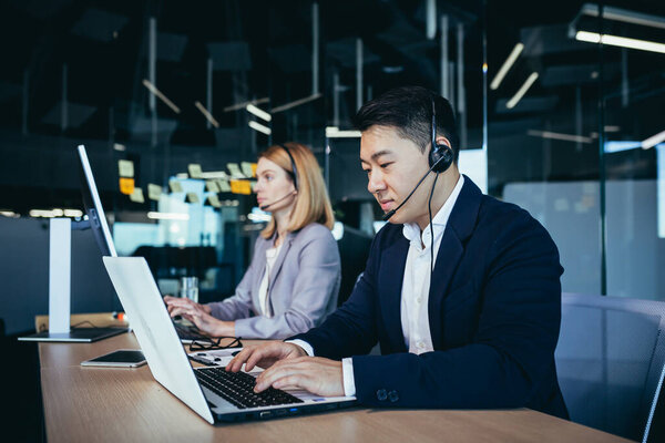 Happy call center employee communicates with customers, advises on video call, remotely, asian business man