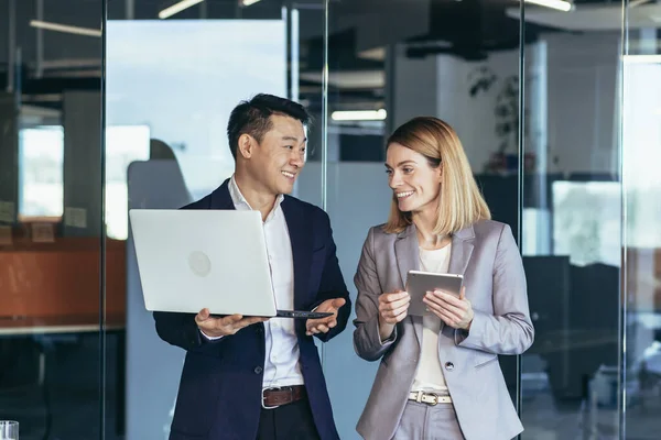 A group of business people stand in the hallway and discuss about problems in the company. Person employees using laptop and digital tablet in office. Thoughtful asian busy managers keeping gadget