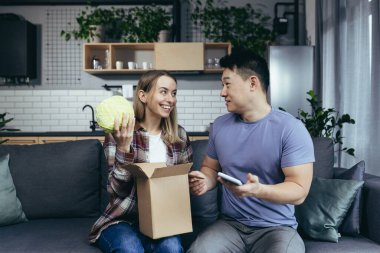 Genç mutlu çift bir paket aldı, online mağazadan alışveriş yapmaktan mutlu ve memnun, erkek ve kadın evde kanepede oturuyor.