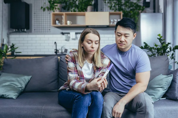 Young couple at home frustrated showing negative doctor pregnancy test, online doctor consultation, man and woman together at home trying to get pregnant