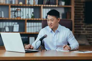 Asyalı serbest yazar ses yayınlarını kaydeder, işadamı ofiste çalışır, profesyonel mikrofon ve dizüstü bilgisayar kullanır